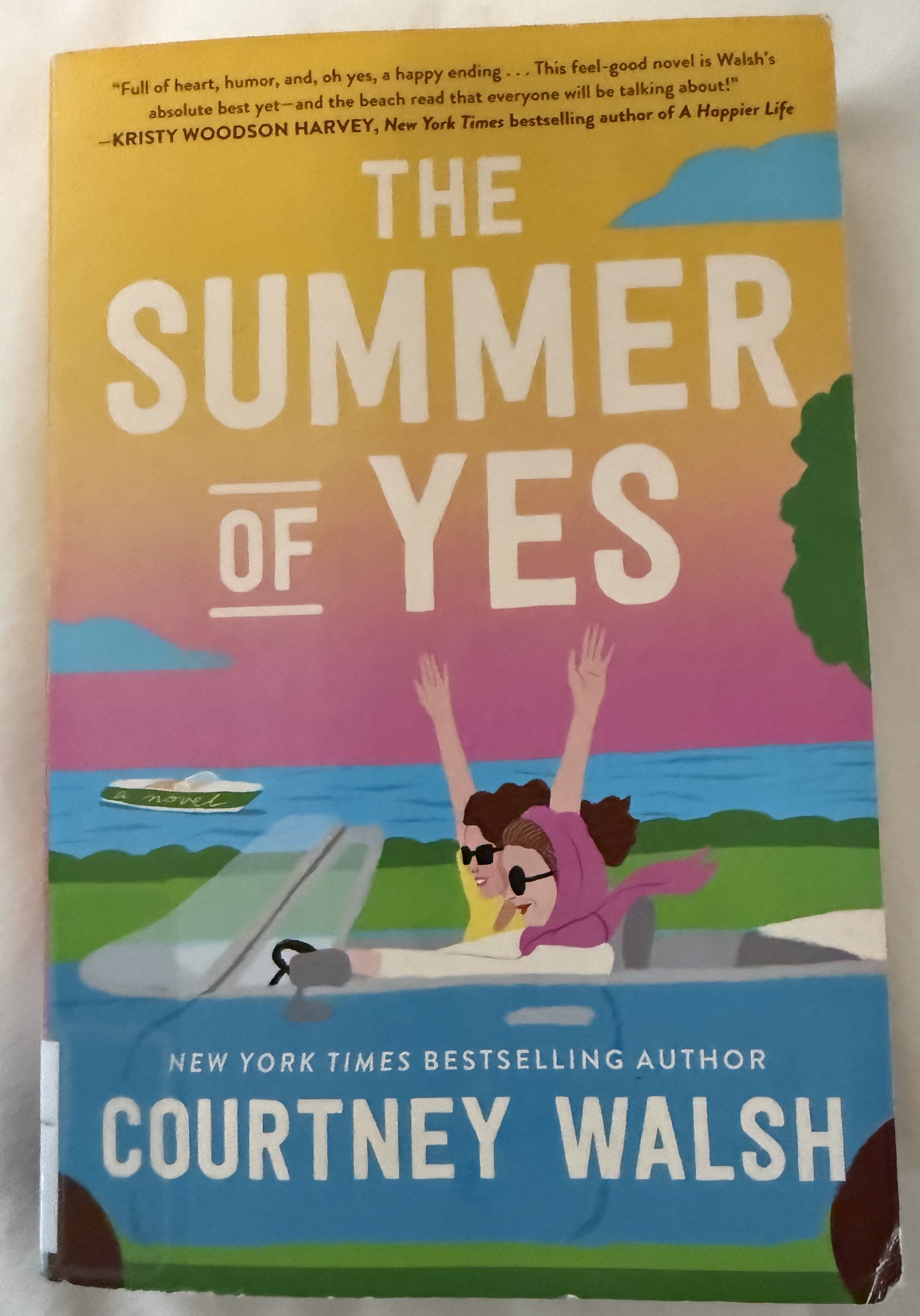Cover of the novel 'The Summer of Yes' by Courtney Walsh, featuring two women in sunglasses joyfully driving in a convertible by the beach with vibrant colors in the background.