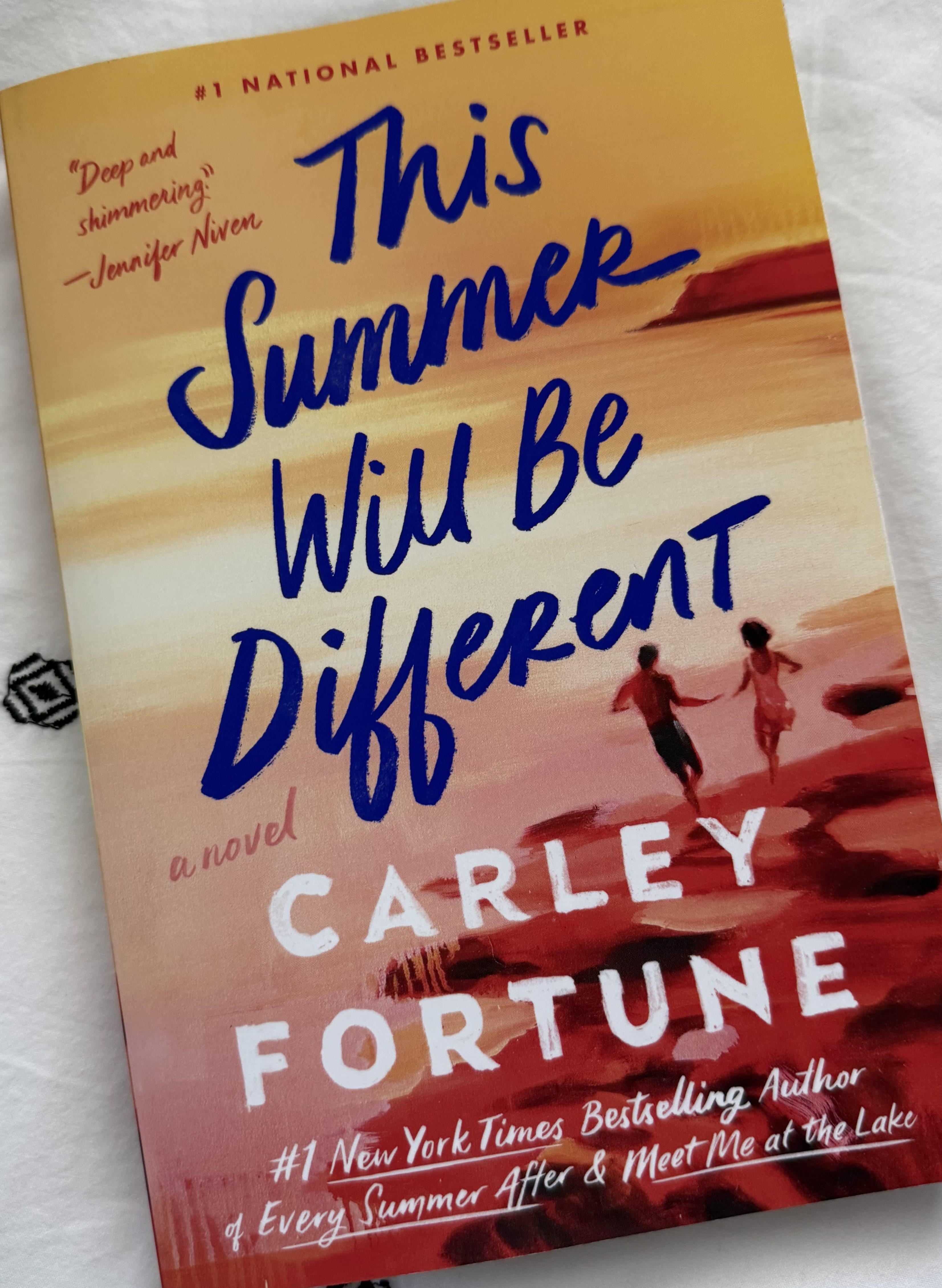 Cover of the novel 'This Summer Will Be Different' by Carley Fortune featuring a sunset background and two figures running along a beach.
