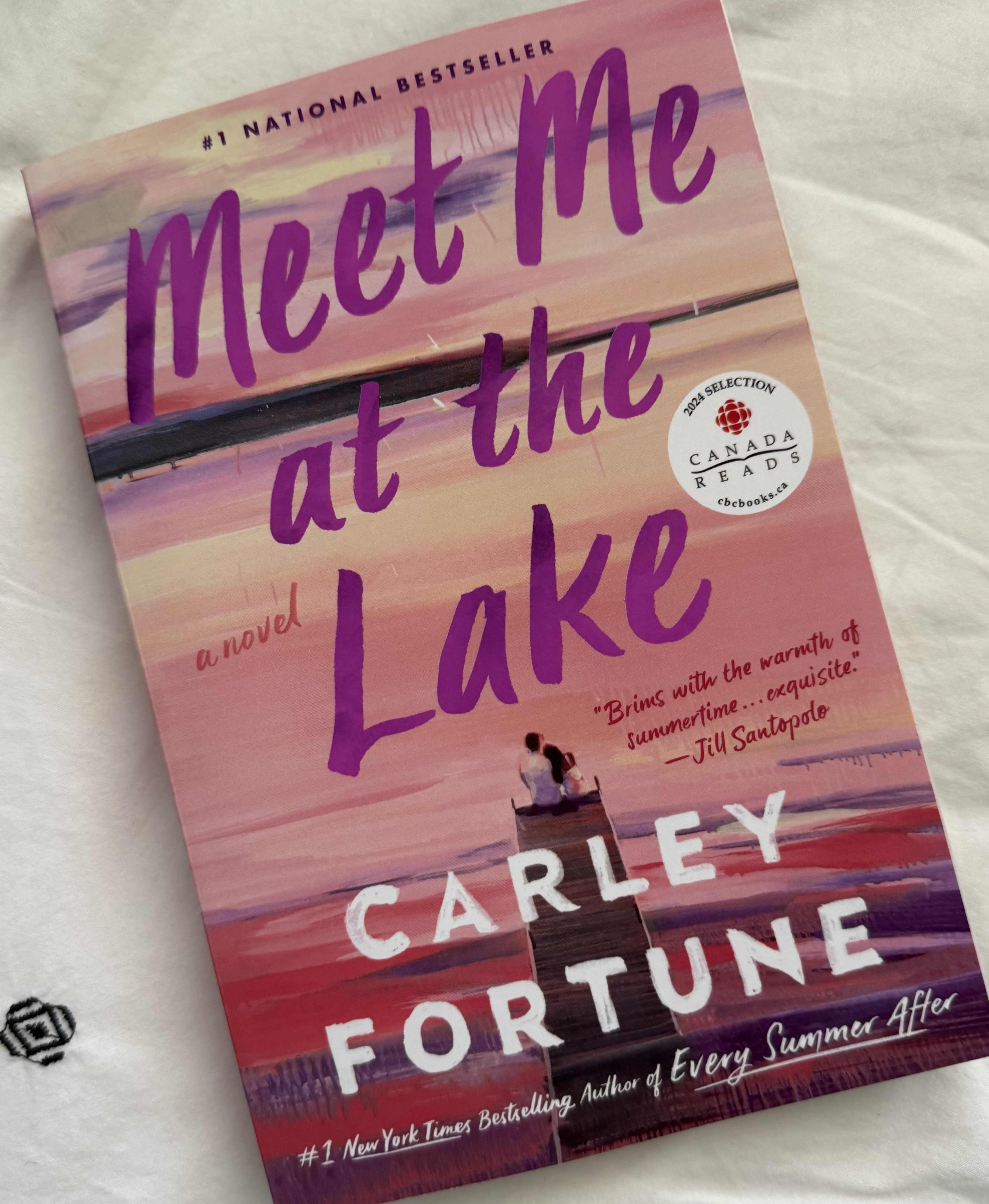 Cover of the novel 'Meet Me at the Lake' by Carley Fortune, featuring a couple sitting on a dock at sunset, with warm colors and artistic text overlay.